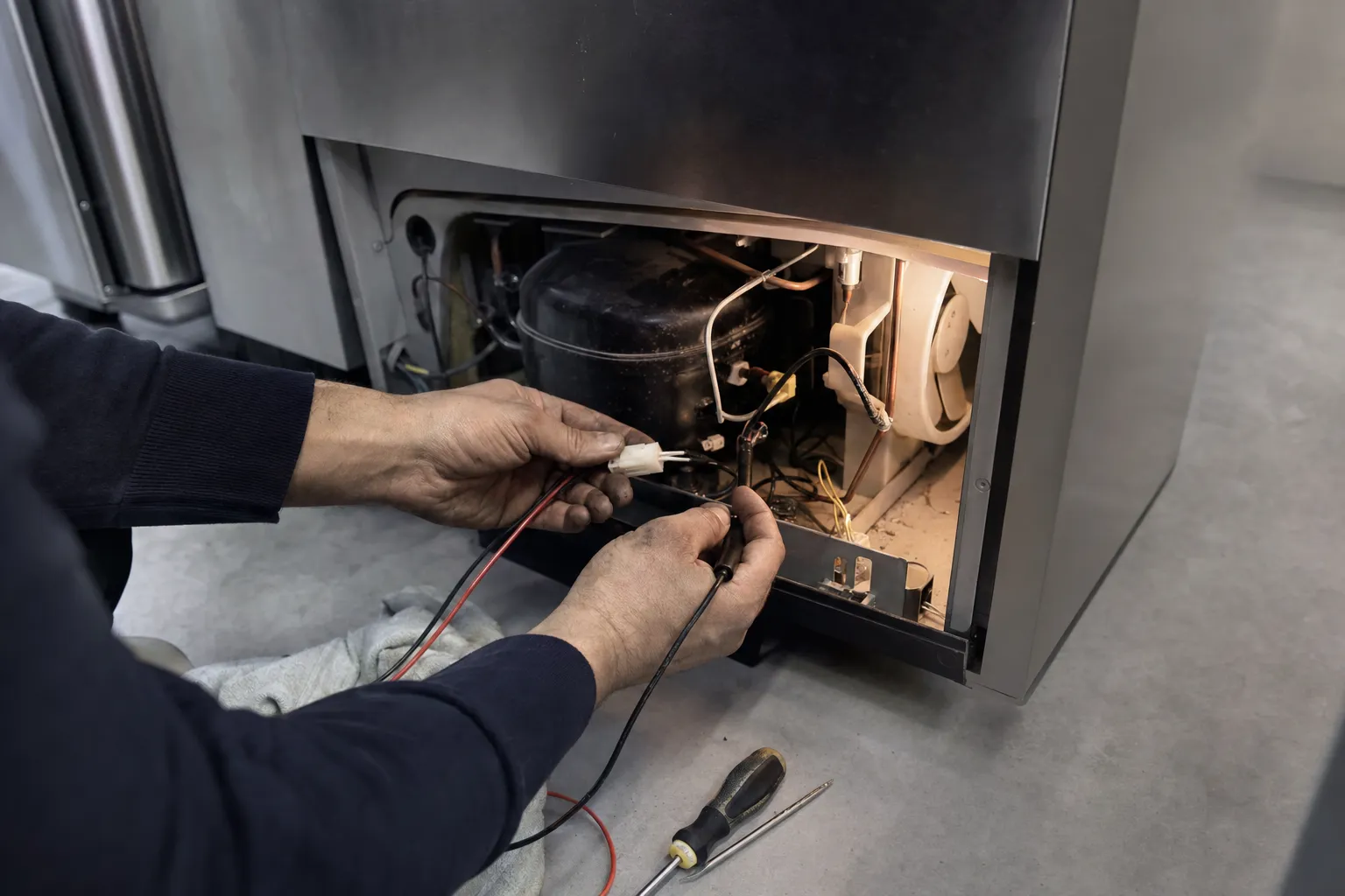 Multimeter probes on a wiring connector next to the compressor and fan shroud in an open lower bay